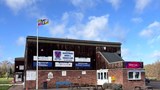 The Bedfordshire flag raised above Biggleswade rugby club. The flag's yellow and red quadrants are taken from the arms of the Beauchamp family, powerful in the county after the Norman conquest of England and constructors of Bedford Castle. The blue and white wavy lines symbolise the Great Ouse, which flows through the county. The three shells are taken from the coat of arms of the Duke of Bedford.